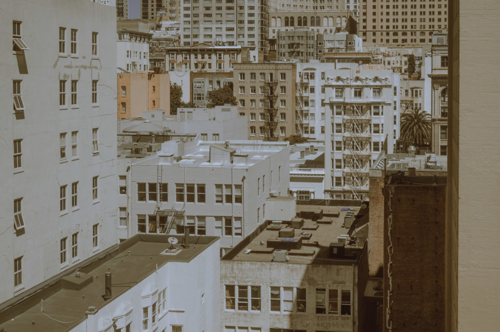 The city unfolds like a densely woven tapestry, each thread representing a mid-rise building standing tall and resolute. The architecture, an eclectic blend of the venerable and the contemporary, tells stories in brick and glass. Facades whisper tales of eras gone by alongside whispers of present ambitions. Under a mercilessly clear sky, the scene bathes in sepia—suffusing the landscape with nostalgia. It feels almost cinematic—a moment caught between past and future—amidst the bustling stillness of daytime.