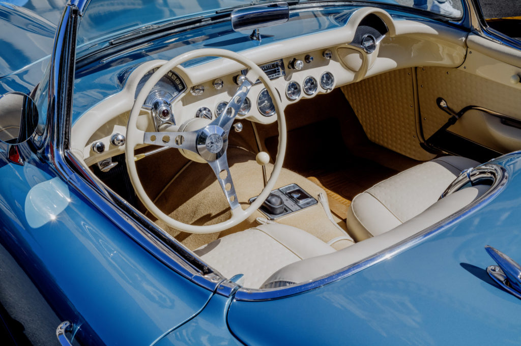 The interior of the convertible hummed with a nostalgic elegance, draped in a delicate dance of cream and white. The dashboard, meticulously crafted, bore an array of gauges that whispered tales from another era. Each dial, each needle spoke of time passed and adventures taken. The steering wheel stood out with its chrome accents, catching the light like bits of morning sun filtering through lace curtains.

The seats carried a sense of history within every stitch—upholstered in a quilted pattern that hinted at care and craftsmanship now rare to find. One could almost hear the soft murmurings of passengers past as they leaned back into its welcoming embrace.

Beyond these gentle confines rested the exterior – an ethereal light blue – reflecting the sky’s serenity on a midsummer afternoon. This car was more than just metal and fabric; it was a tender evocation of stories yearned to be relived, journeys eager to be revisited.